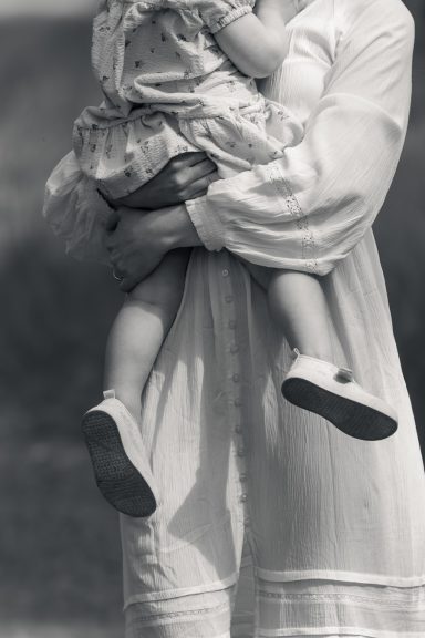 Svartvitt foto med cinematic stil föreställande ett barns ben som hänger ner framför mamma som bär barnet, Anna Esmelöv