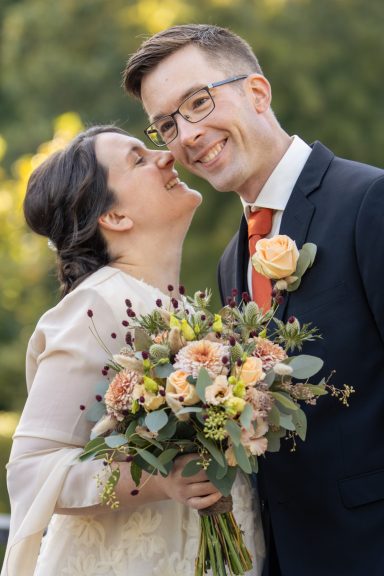Bruden får brudgummen att skratta genom att viska något i hans öra, poser för bröllopsfoto av Anna Esmelöv
