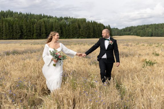 Brudpar håller hand när de går på en åker på bröllop i lantlig miljö mellan Norrköping och Söderköping, fotograf Anna Esmelöv