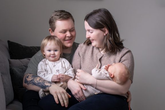 Familjeporträtt av dokumentär lifestyle stil där familjen skrattar och håller om varandra i naturligt ljus inomhus, familjefotograf Esmelöv