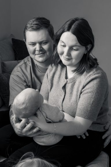 Föräldrar håller och tittar kärleksfullt på sitt lilla barn, svartvitt foto i naturligt ljus inomhus, familjefotograf Anna Esmelöv