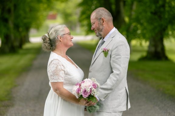 Brudpar står i allé och tittar varandra i ögonen, bröllop i Kvistrum utanför Åtvidaberg, porträttfotograf Anna Esmelöv