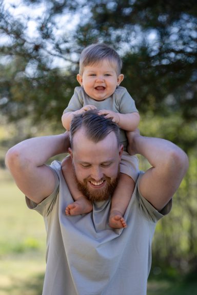 Spontan bild där barn rider på pappas axlar utomhus, fotograferad i naturligt ljus av familjefotograf Anna Esmelöv Östergötland