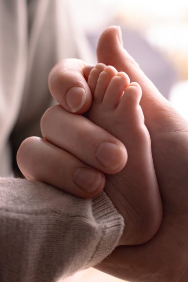 Detaljbild av en liten bebisfot i mammas hand, storytelling familjefotografering inomhus i naturligt ljus, Anna Esmelöv